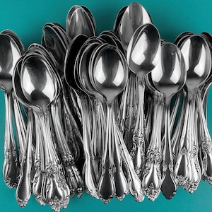 May include: A large group of silver spoons with ornate handles. The spoons are arranged in a fan shape, with the handles pointing outwards.