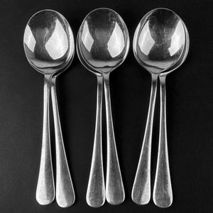 May include: Three silver spoons with rounded bowls and long handles. The spoons are arranged in a row, with the handles pointing upwards.