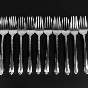 May include: A set of 12 silver cake forks with ornate handles. The forks are arranged in a row on a black background.