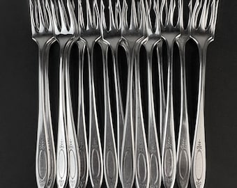 May include: A set of ten silver forks arranged in a row against a black background. Each fork has a long, slender handle with an oval design and decorative detailing. The tines are pointed and evenly spaced.