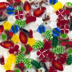 May include: A collection of colorful, decorative glass pieces in various shapes, including strawberries, stars, Christmas trees, and gift boxes. The pieces are red, green, yellow, white, and blue, with some resembling holiday themes.