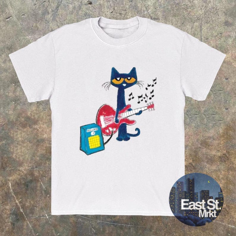 May include: White t-shirt with a cartoon cat playing a red guitar and a blue amplifier. The cat is dark blue with yellow eyes. Musical notes float above the guitar. The shirt has the text "East St. Mrkt" in a circle.
