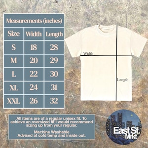May include: Cream-coloured unisex t-shirt with measurements in inches. Sizes range from S (45.7cm width, 71.1cm length) to XXL (66cm width, 81.3cm length). The shirt is machine washable and advised to be washed cold and inside out. The East St. Mrkt logo is in the bottom right.