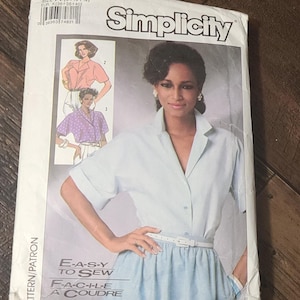 May include: Simplicity sewing pattern 7482 featuring a woman in a light blue collared shirt and skirt. The pattern includes instructions for an easy-to-sew design. The package also shows two other shirt designs. The text "E-A-S-Y TO SEW" is visible.