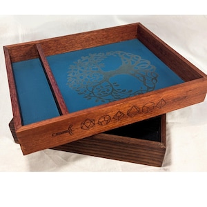 May include: A wooden dice tray with a blue interior and a tree of life design. The tray has a dark wood finish and etched dice symbols and a sword. Designed for tabletop gaming, it is a practical accessory.