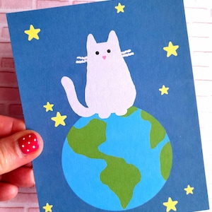 Carte chat assis sur la Terre , dominant le monde  , carte postale chat dans l'espace  , carte chat mignon .