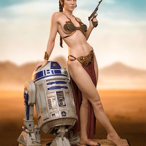 Könnte beinhalten: Eine detaillierte Statue einer Frau in einem goldenen Bikini, die einen Blaster hält und sich an einen R2-D2-Droiden lehnt. Die Statue ist vor einer Wüstenkulisse platziert, wobei die Kleidung der Frau und das Design des Droiden ein Science-Fiction-Thema hervorrufen.