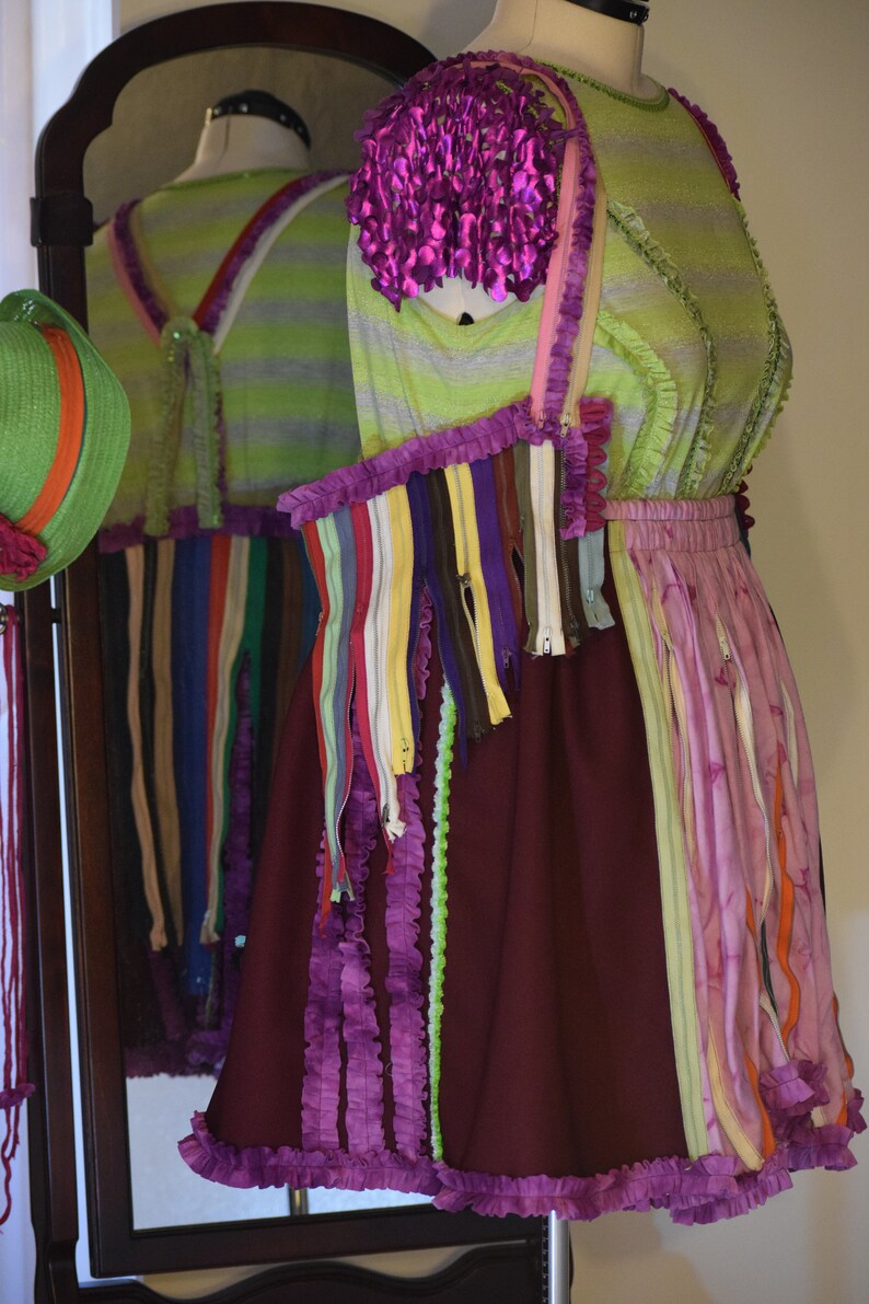 May include: A purple, green, and brown dress with a ruffled hem and a variety of colorful zippers and fabric strips. The dress is made from recycled materials and has a unique, handmade aesthetic.