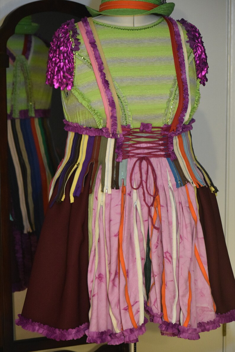 May include: A pink and burgundy dress with a green striped bodice and a skirt made of colorful zippers. The dress has a purple ruffle trim and a lace-up back.