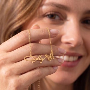 May include: A gold-toned necklace featuring a delicate chain and a personalized nameplate pendant that reads Polly in a cursive script font, accompanied by a small, intricate butterfly charm attached to the right side of the name.