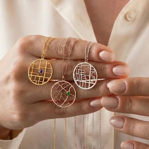 May include: Three round pendant necklaces with chain. One is gold with a blue gem, one is rose gold with a green gem, and one is silver. The pendants feature a map design.