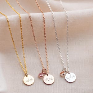 Peut inclure: Quatre colliers délicats en or, or rose et argent. Chaque collier est composé d'une fine chaîne et d'un petit pendentif rond gravé d'un nom. Certains pendentifs ont une petite pierre précieuse. Les colliers sont présentés sur un tissu doux de couleur neutre.
