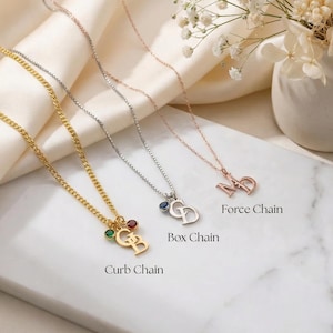 Può includere: Una selezione di collane personalizzate in oro, argento e oro rosa. Ogni collana presenta un ciondolo con iniziali e pietre preziose. L'immagine mostra tre stili di catena: Curb, Box e Force. Il testo recita "Curb Chain", "Box Chain" e "Force Chain".