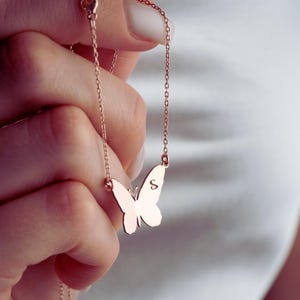 May include: A rose gold-toned necklace featuring a delicate chain and a butterfly-shaped pendant. The butterfly charm has a smooth, polished surface with the letter S engraved on one of its wings, suspended from a thin, matching metal link chain.
