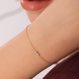Op de afbeelding: Een delicate gouden kettingarmband met een enkele, kleine, rechthoekige paarse edelsteen.