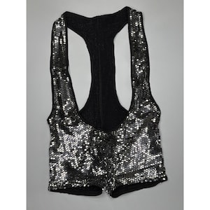 Può includere: Un gilet nero con paillettes e design a vogatore. Il gilet è ricoperto di piccole e lucenti paillettes che riflettono la luce. Ha uno scollo tondo e una silhouette aderente.
