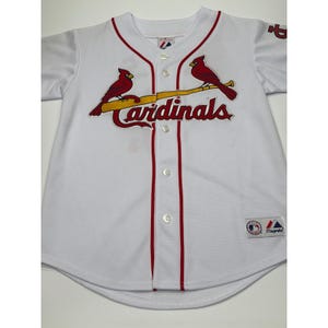 May include: White baseball jersey with red trim and the word "Cardinals" in red script. Two red cardinal birds are perched on a yellow baseball bat. The jersey has a button-up front and short sleeves.