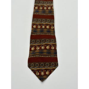 May include: A patterned necktie with a repeating design of brown circles, gold moons, and horizontal stripes. The tie is primarily burgundy with accents of gold, brown, and navy blue. The tie is displayed on a white background.