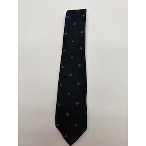 Op de afbeelding: Een donker marineblauwe stropdas met een herhalend patroon van kleine, felgroene klaverbladpictogrammen die gelijkmatig over de stof zijn verdeeld. De das heeft een puntig uiteinde en een gladde, matte afwerking met een consistente print.