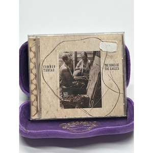 May include: A CD case with the album "Common Thread: The Songs of the Eagles" inside a purple velvet case. The CD cover features a sepia-toned image of two people and the text "Common Thread:" and "The Songs of the Eagles".