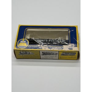 May include: A model train set in its original box. The box is yellow and blue with the text "AHM" and "THE FINEST TOYS FROM AHM ASSOC." The box contains a black train model. The box also features images of different train models.