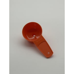 May include: An orange plastic measuring cup with a handle and a hole for hanging. The cup has a rounded bowl shape and is designed for measuring dry or liquid ingredients. The handle has a hole for easy storage.