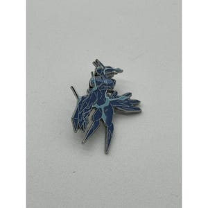 Pode incluir: Um alfinete de metal azul e prateado em forma de criatura estilizada. O alfinete apresenta um design detalhado com um corpo azul escuro e detalhes em azul claro. O alfinete é provavelmente um item de colecionador ou decorativo.