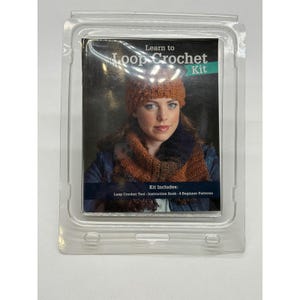 May include: A Learn to Loop Crochet Kit in clear plastic packaging. The product label features a person wearing a textured orange beanie and a dark blue and orange scarf. Text on the label reads: Learn to Loop Crochet Kit, Kit Includes: Loop Crochet Tool, Instruction Book, 4 Beginner Patterns.