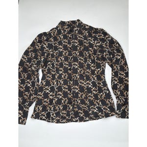 May include: Black button-down shirt with a repeating gold and tan chain-link pattern. The long-sleeved shirt has a high collar and buttoned cuffs. The shirt is made of a lightweight material.