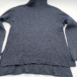 May include: A dark gray turtleneck sweater with long sleeves. The sweater has a ribbed knit texture and a split hem design. The sleeves are wide and flared. The sweater is made of a soft, comfortable material.