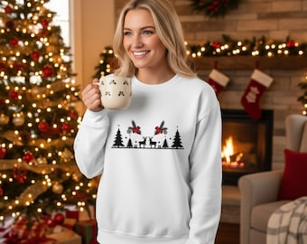 May include: White sweatshirt with a black Christmas design featuring trees, reindeer, and bows. The woman is holding a mug with a pattern of small black shapes. A Christmas tree and fireplace are in the background.