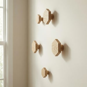 May include: A set of five wooden wall hooks in a natural wood finish. The hooks have an octagonal design and are mounted on a light-colored wall. The hooks are of varying sizes and shapes, offering a modern, minimalist aesthetic.