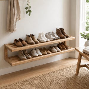 May include: A two-tiered wooden shoe rack mounted on a white wall, displaying various shoes. The top shelf holds boots and sneakers, while the bottom shelf features loafers and flats. A neutral-toned rug and a small wooden bench are in the foreground.
