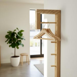 Op de afbeelding: Houten wandkapstok met een rechthoekig frame en meerdere haken. Twee houten kleerhangers hangen aan een horizontale stang. De kapstok is gemaakt van lichtgekleurd hout.