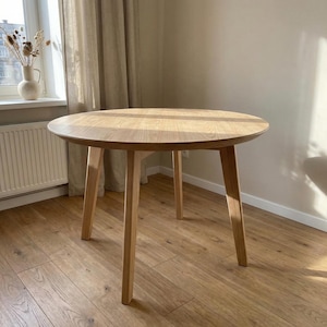 Könnte beinhalten: Ein runder Holztisch mit heller Eichenholzoberfläche. Der Tisch hat eine glatte Oberfläche und vier abgewinkelte Beine. Der Tisch hat einen Durchmesser von ca. 91 cm und eignet sich für ein Ess- oder Wohnzimmer.