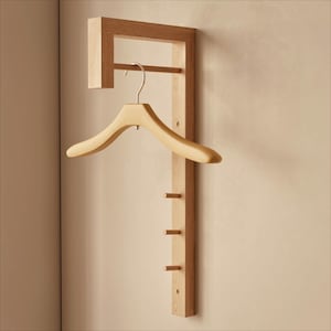 Op de afbeelding: Een houten wandgarderobe met een ingebouwde hanger en drie haken. De garderobe is gemaakt van lichtgekleurd hout en heeft een houten hanger. Het ontwerp is minimalistisch en functioneel, geschikt voor entrees of slaapkamers.