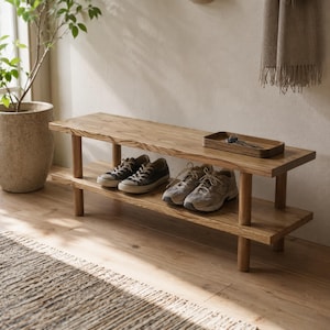 Puede incluir: Un banco zapatero de madera de dos niveles con acabado en marrón claro natural, que cuenta con cuatro patas cilíndricas y dos estantes rectangulares. Una pequeña bandeja de madera con llaves de metal descansa sobre la superficie.