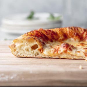 Puede incluir: Primer plano de una rebanada de pizza con una corteza crujiente y queso derretido. La pizza está sobre una tabla de cortar de madera.