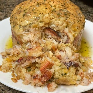 Può includere: Un primo piano di un piatto di granchio al forno con una crosta dorata e una salsa cremosa. La polpa di granchio è visibile all'interno del piatto e parte di essa è caduta sul piatto.
