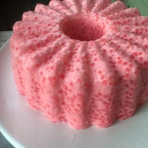May include: A pink gelatin dessert with a ring shape and a textured surface. The dessert is made with tapioca pearls and is on a white plate.