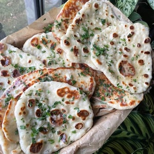 Peut inclure: Un panier de pain naan fraîchement cuit garni de persil haché. Le naan est doré et légèrement gonflé, avec une texture croustillante.