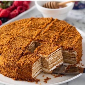 Könnte beinhalten: Ein mehrschichtiger Honigkuchen, auch bekannt als Medovik, ist in Scheiben geschnitten und bereit zum Servieren. Der Kuchen ist mit einer Streusel-Topping bedeckt und hat eine hellbraune Farbe.