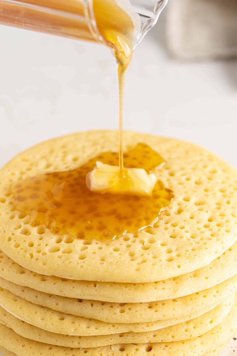 Może przedstawiać: Stos złotych, brązowych naleśnik&oacute;w polanych miodowym syropem i ozdobiony kawałkiem masła.