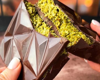 May include: A geometric chocolate dessert, broken open to reveal a green filling. The dark chocolate exterior has a faceted design. The filling appears to be a textured, light green color.