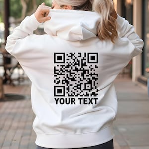 May include: White hoodie with a black QR code and the text "YOUR TEXT" printed on the back.