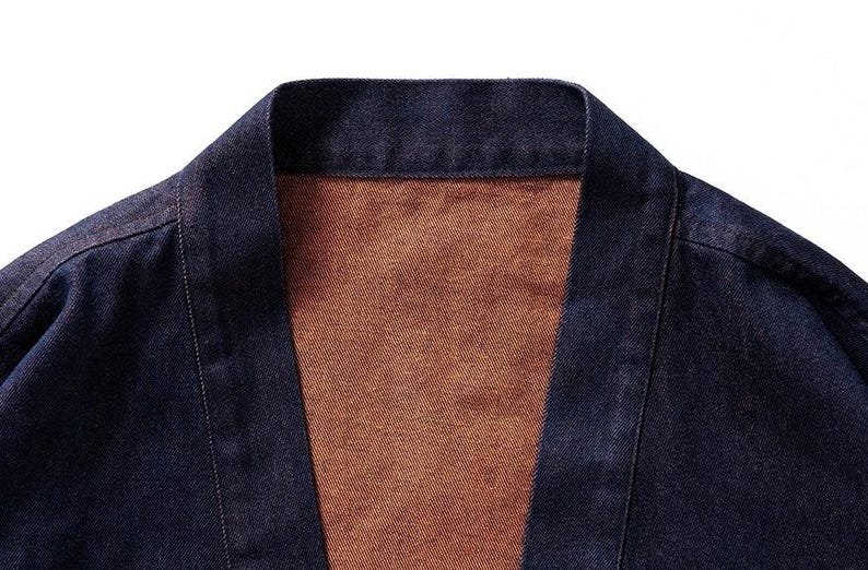 May include: A dark blue denim jacket with a brown lining. The jacket has a traditional Japanese style with a wide collar and a long, open front.