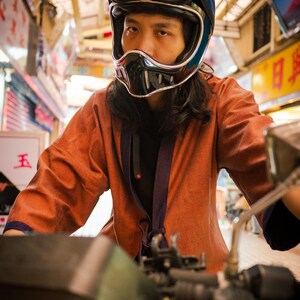 May include: A person wearing a black motorcycle helmet with a visor and a brown jacket. The person is riding a motorcycle.
