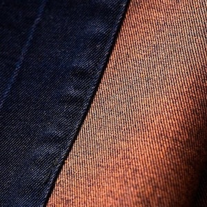 May include: Close-up of two different types of fabric. One is a dark blue denim and the other is a brown denim.