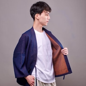 May include: A dark blue denim jacket with a brown lining. The jacket has a traditional Japanese style with a wide collar and a tie closure.
