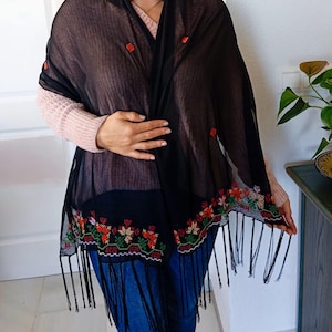 May include: Black sheer shawl with embroidered floral details and fringe trim. The shawl is made of a lightweight fabric and has a delicate, feminine look.